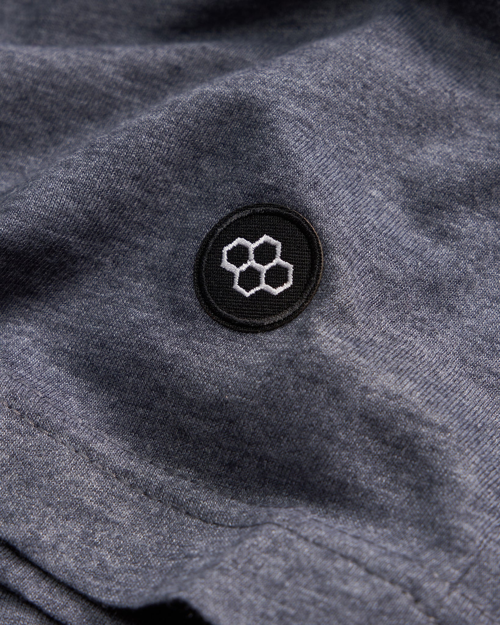 A close-up view of a dark gray fabric with a circular black patch featuring a white honeycomb design