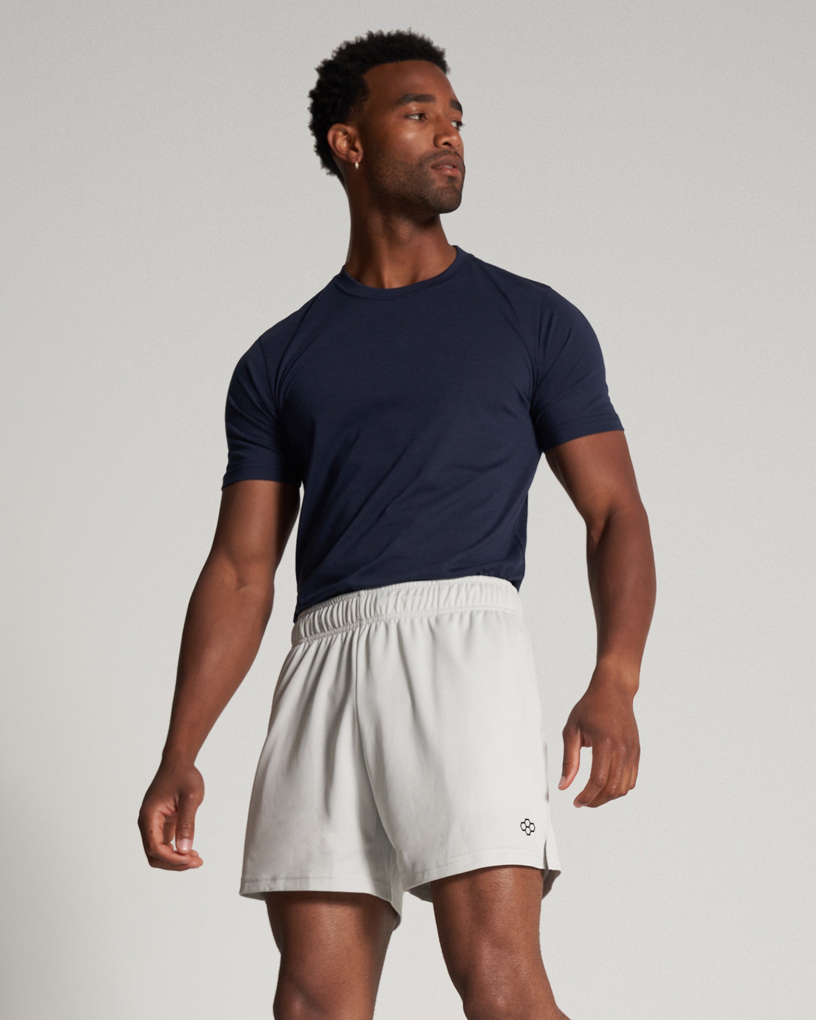 A muscular man poses confidently in a navy athletic t-shirt and light-colored shorts showcasing a modern sporty style