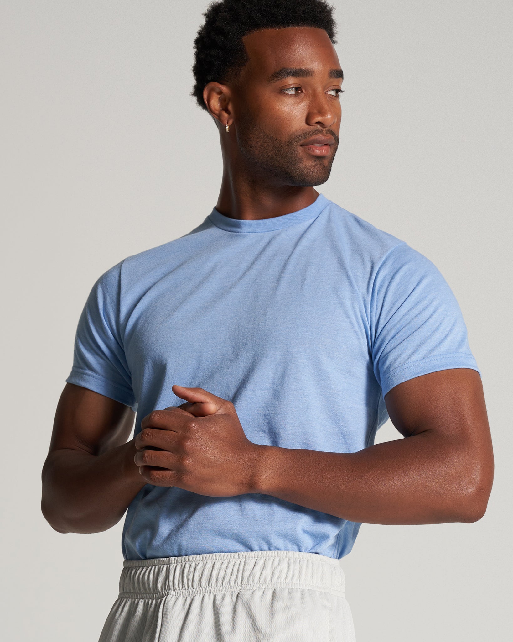 A man wearing a light blue t-shirt and light gray shorts poses confidently against a neutral background highlighting contemporary casual fashion