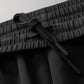 Close-up view of a comfortable black waistband with an adjustable drawstring featuring sleek toggles, set against a subtle gray background.