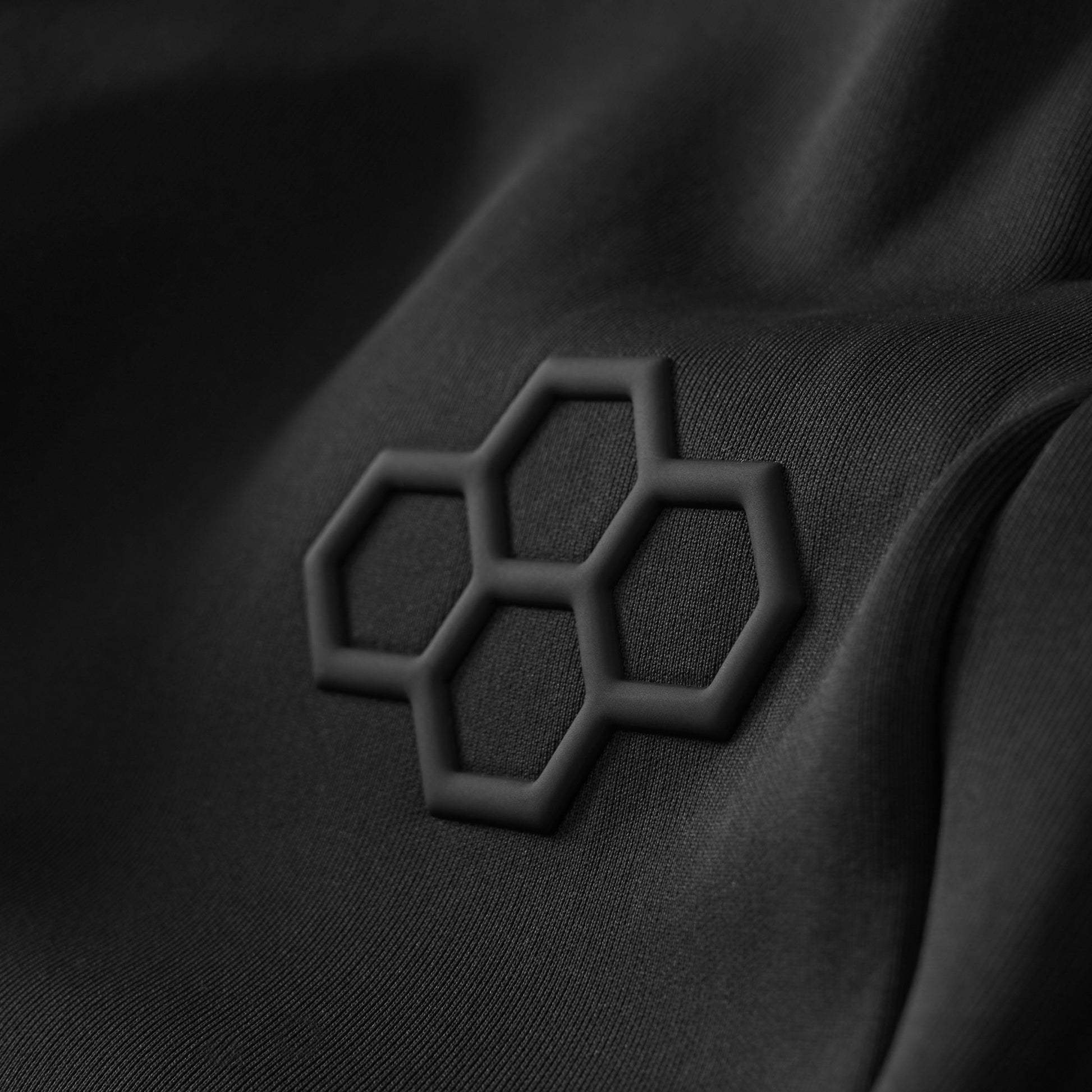 Close-up of textured black fabric showcasing a three-dimensional hexagonal logo, highlighting a modern, minimalist aesthetic.