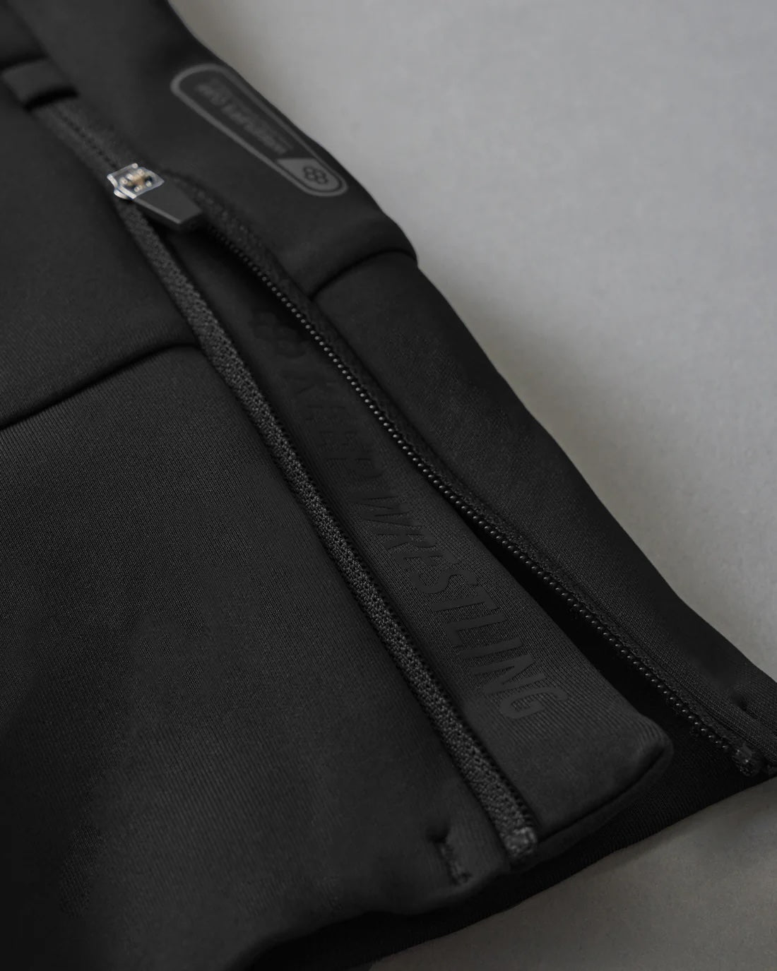 Black fabric with a prominent silver zipper detail, showcasing textured elements for grip against a subtle gray background.