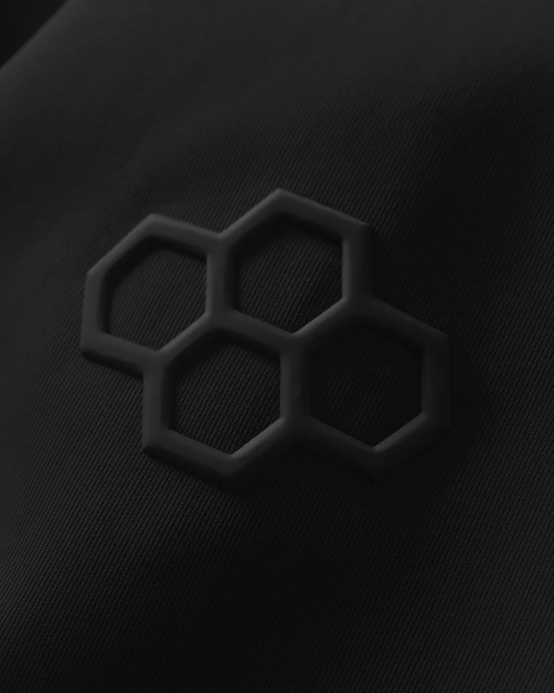 Textured black fabric displays a raised hexagonal logo, combining sleek aesthetics with a durable surface.