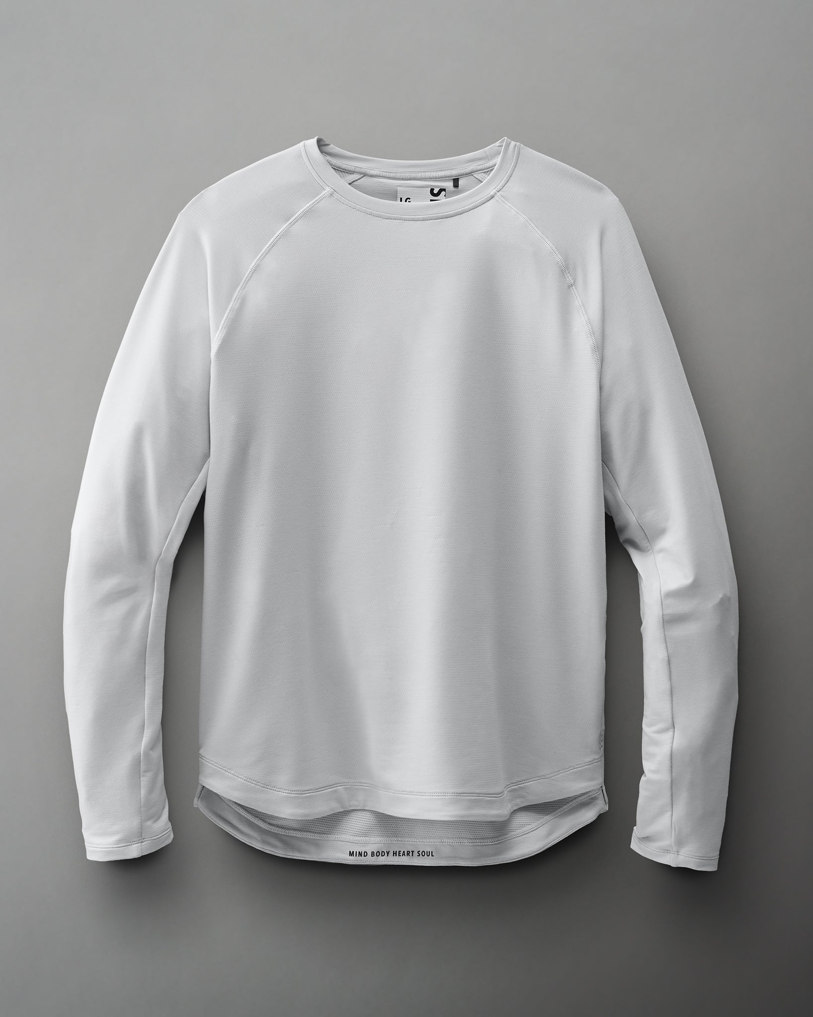 A light gray long-sleeve shirt with a round neckline and raglan sleeves features the phrase 'MIND BODY HEART SOUL' at the hem, highlighting its activewear appeal.