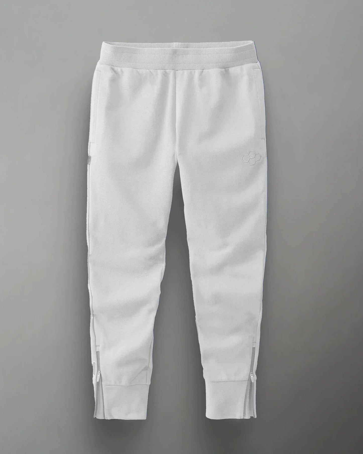 White athletic sweatpants with zippered pockets and ankle zippers for comfort and style, featuring a subtle logo on the left thigh.