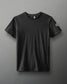 A plain black short-sleeve T-shirt with a smooth texture and a small white emblem on the sleeve, set against a muted gray background.