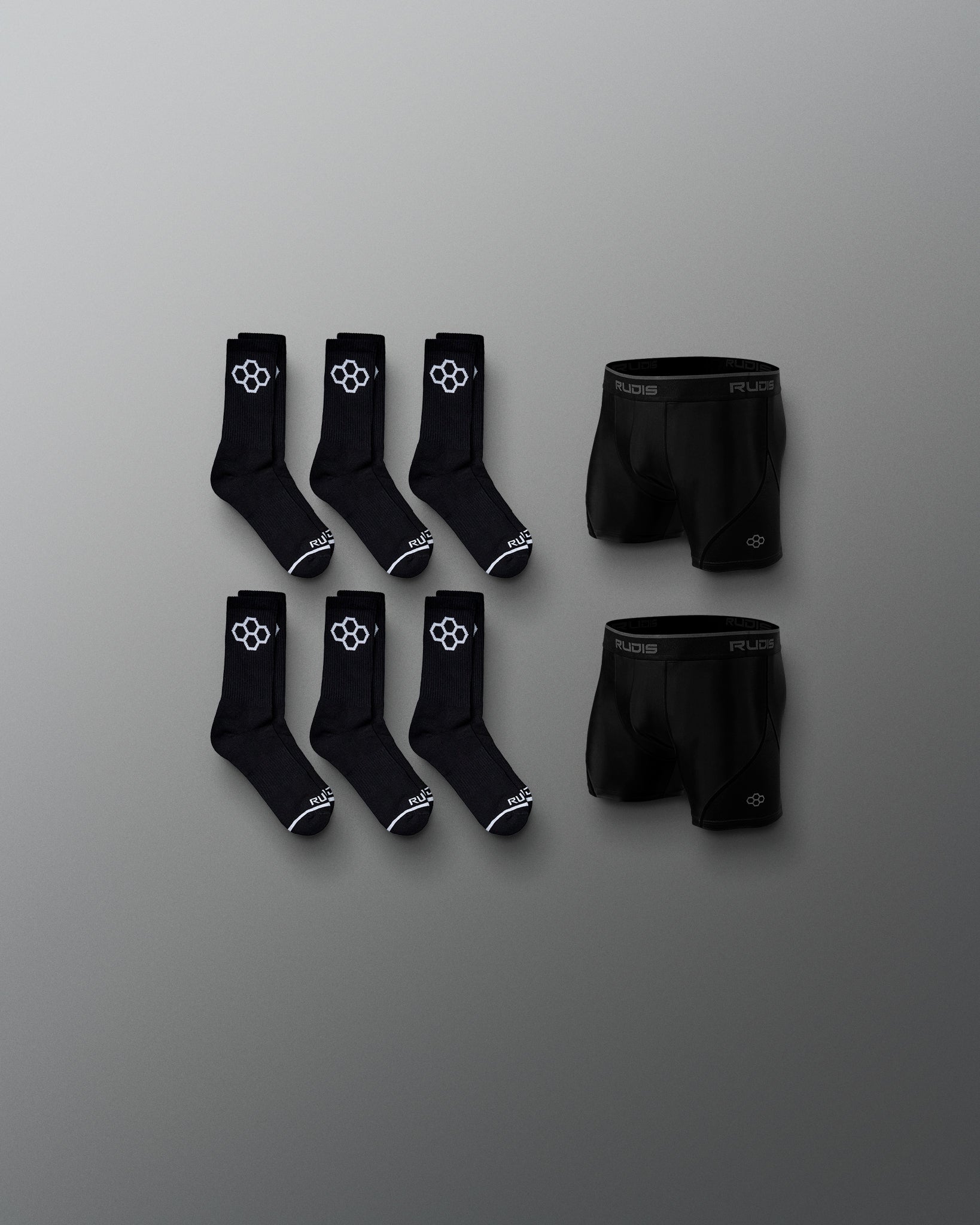 Three pairs of black socks and one pair of black shorts are organized on a gray background, featuring a minimalistic design with white logos.