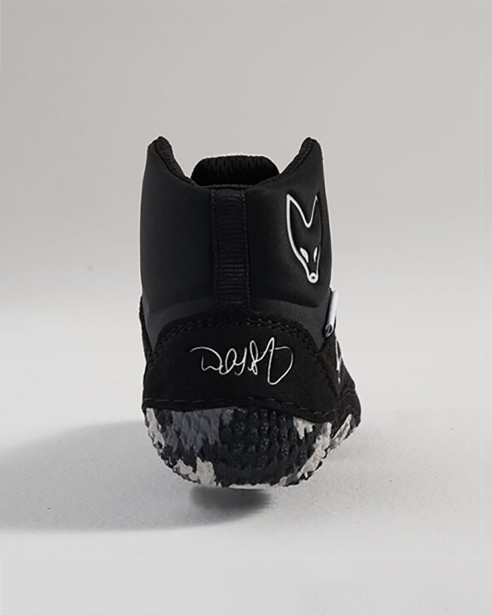 A back view of a sleek black athletic shoe featuring a distinctive logo unique tread pattern and a personalized signature on the heel