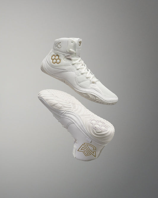 White high-top athletic shoes with modern design elements, gold accents, and textured soles for improved grip, set against a neutral gray background.