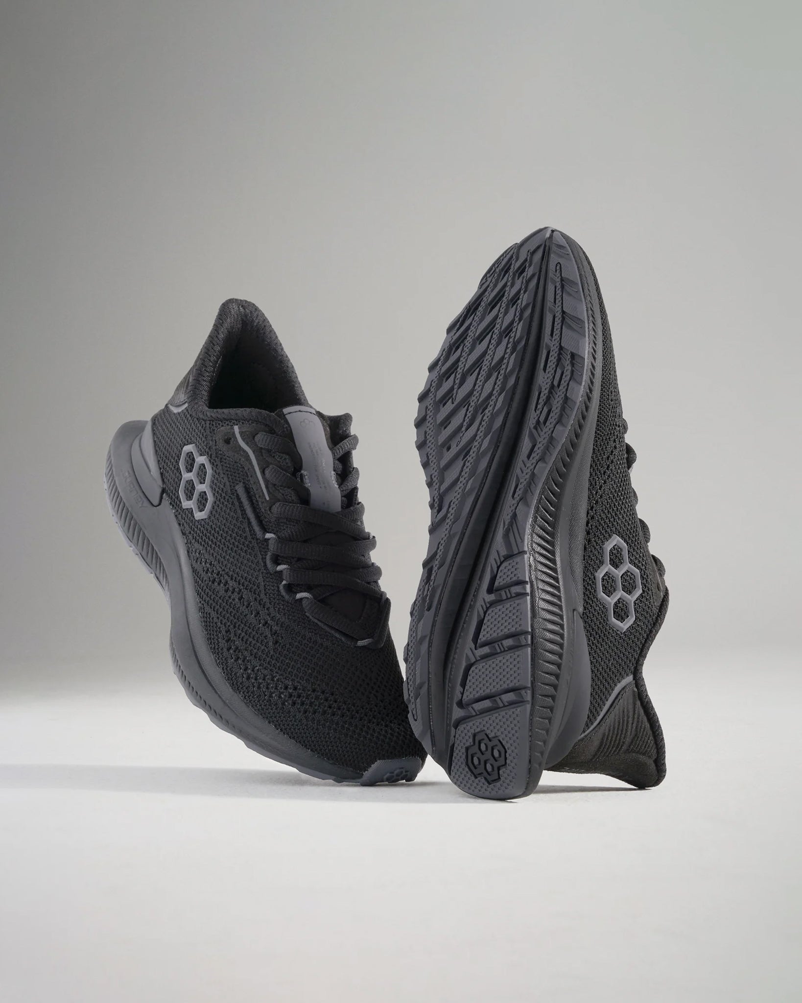 This image presents a pair of sleek black athletic shoes featuring a breathable upper and textured sole showcased from a dynamic angle