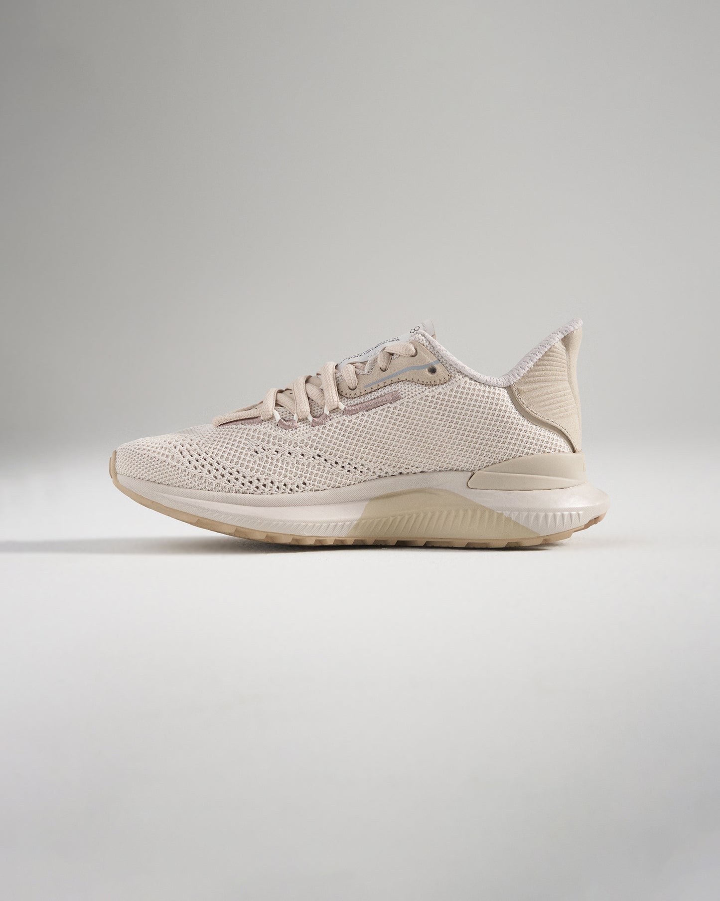 A side view of a light beige athletic shoe featuring a breathable mesh upper designed for comfort and performance