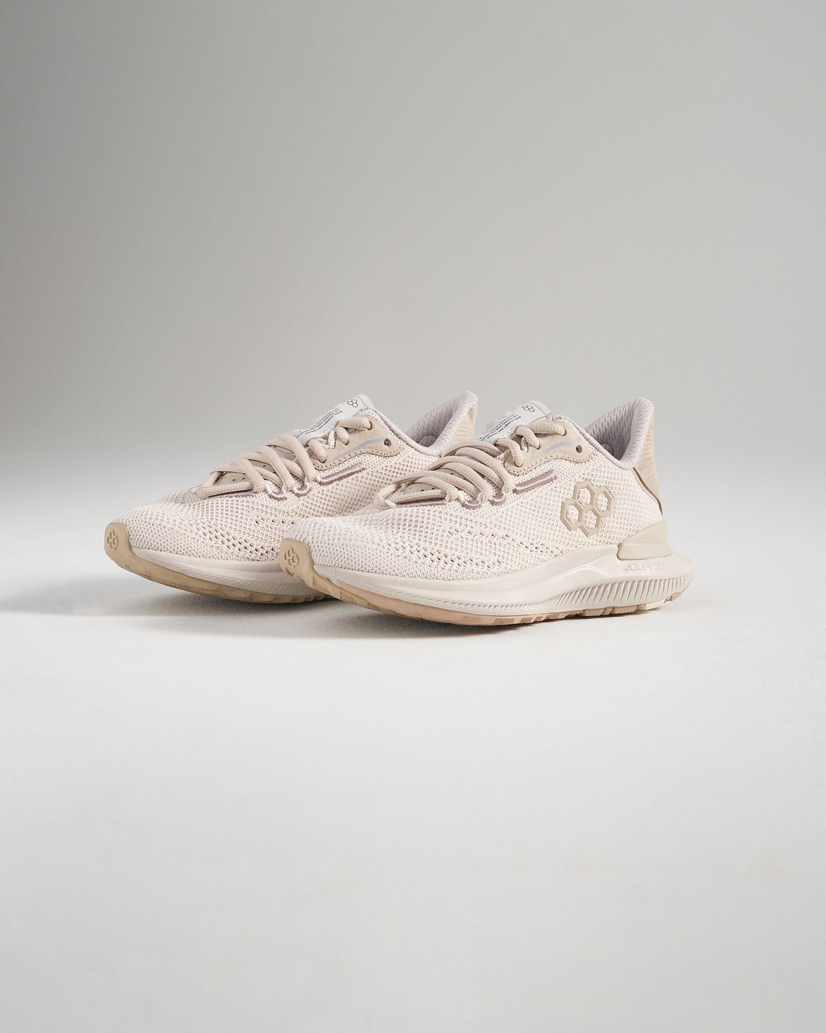 A pair of light beige athletic shoes designed for comfort and performance featuring a textured mesh upper and a supportive sole