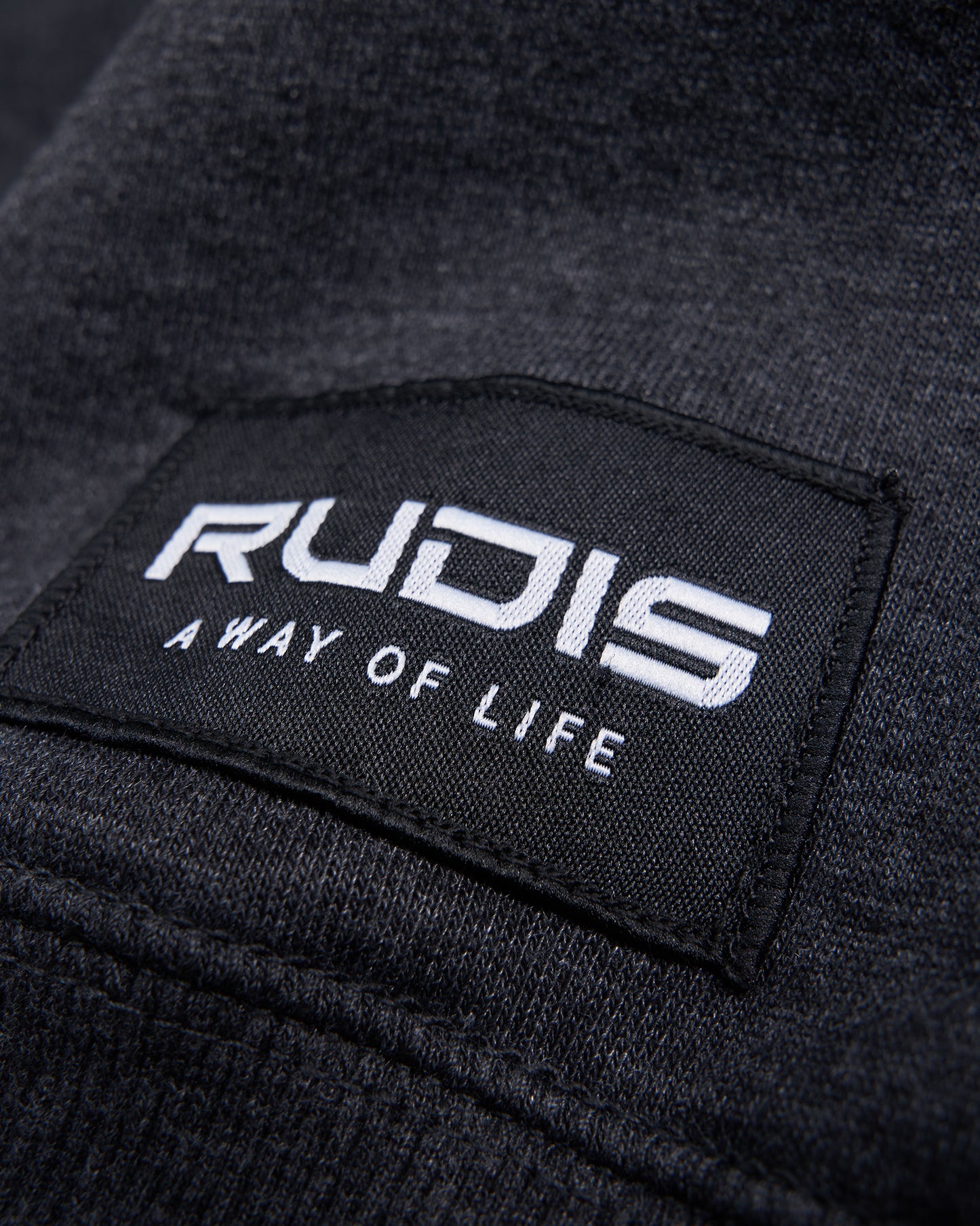 A close-up view of a fabric label featuring the brand name RUDIS and the phrase A WAY OF LIFE in bold white lettering against a black background