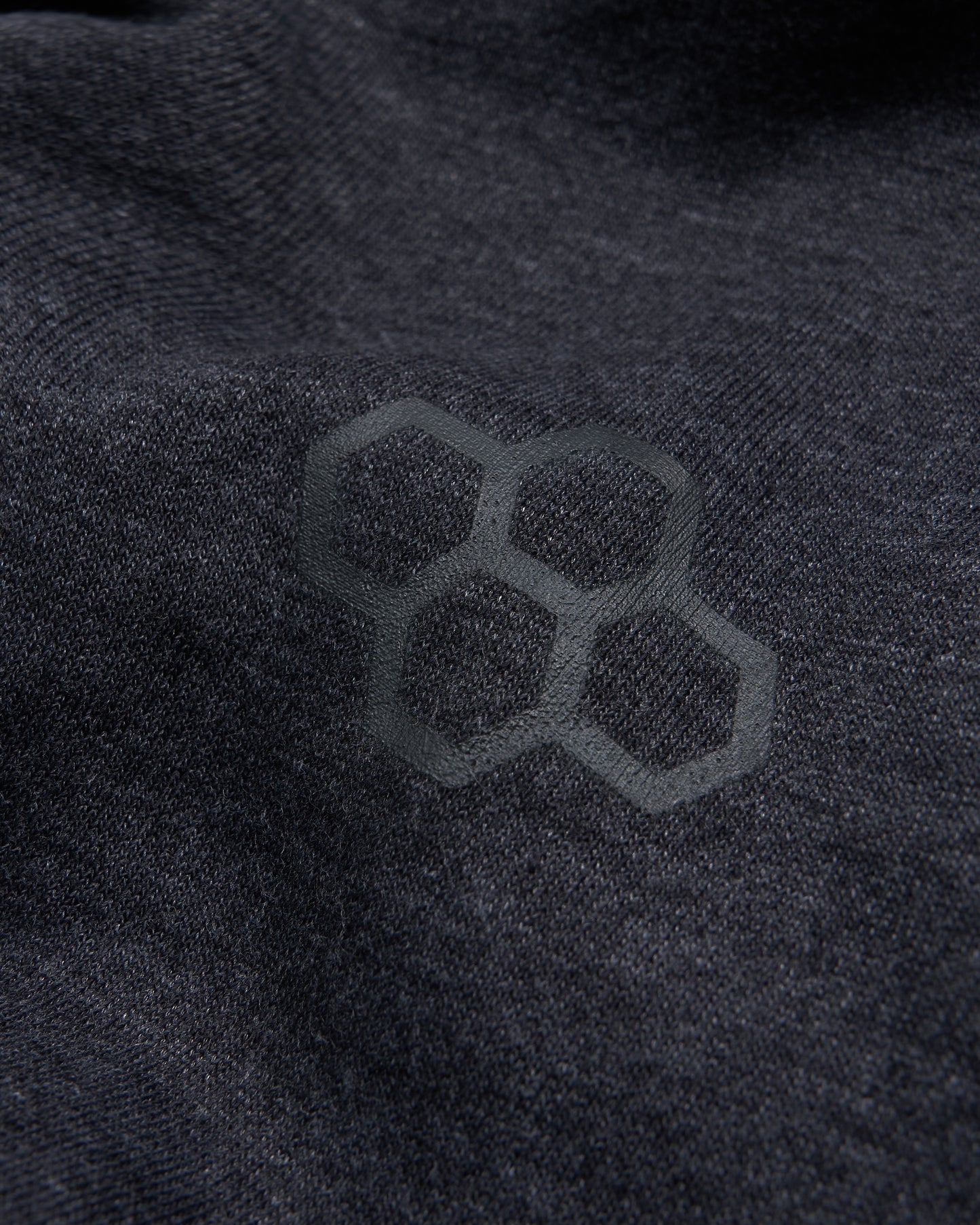 A close-up view of a textured dark fabric featuring a subtle hexagonal logo embossed on its surface