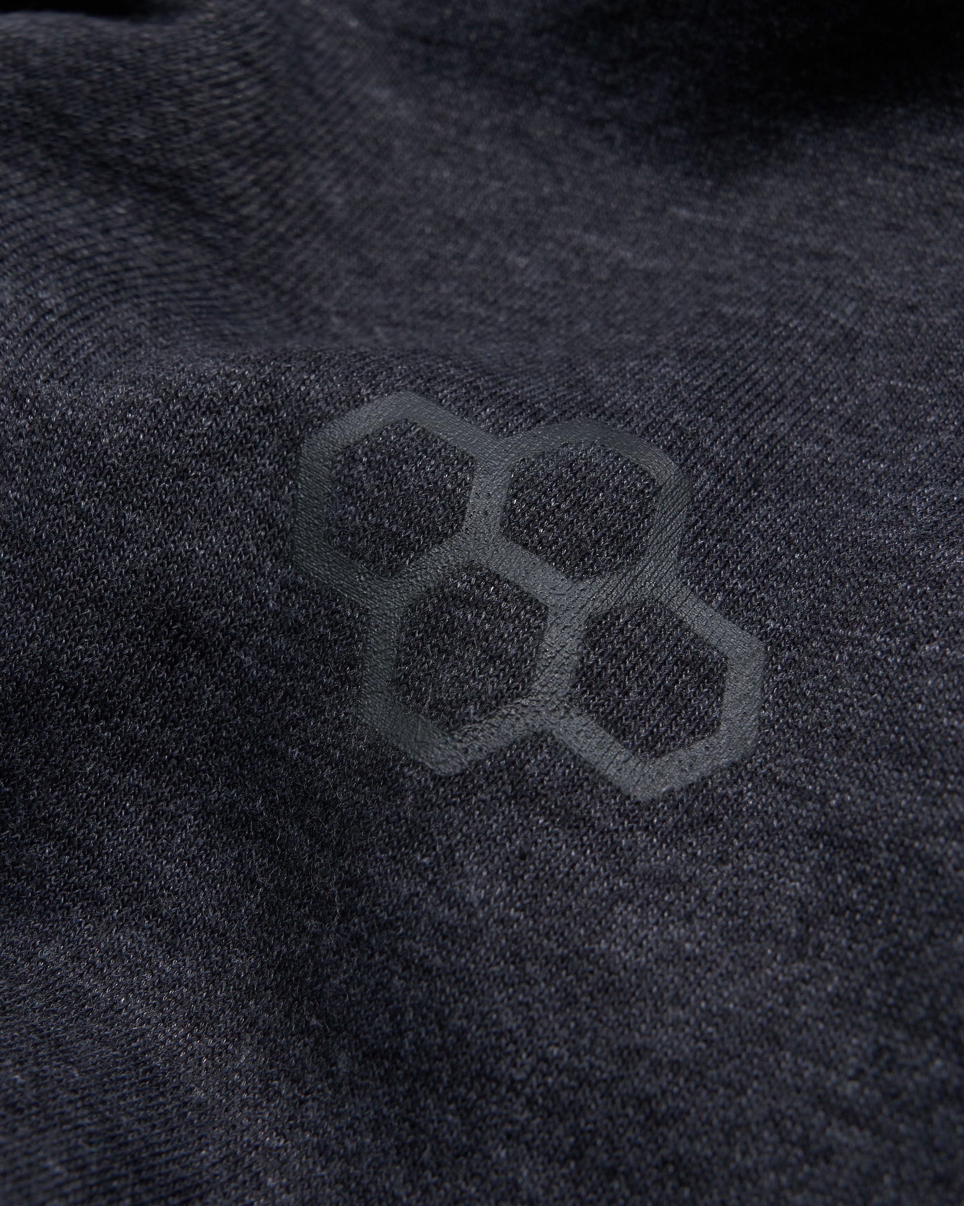 A close-up view of a textured dark fabric featuring a subtle hexagonal logo embossed on its surface