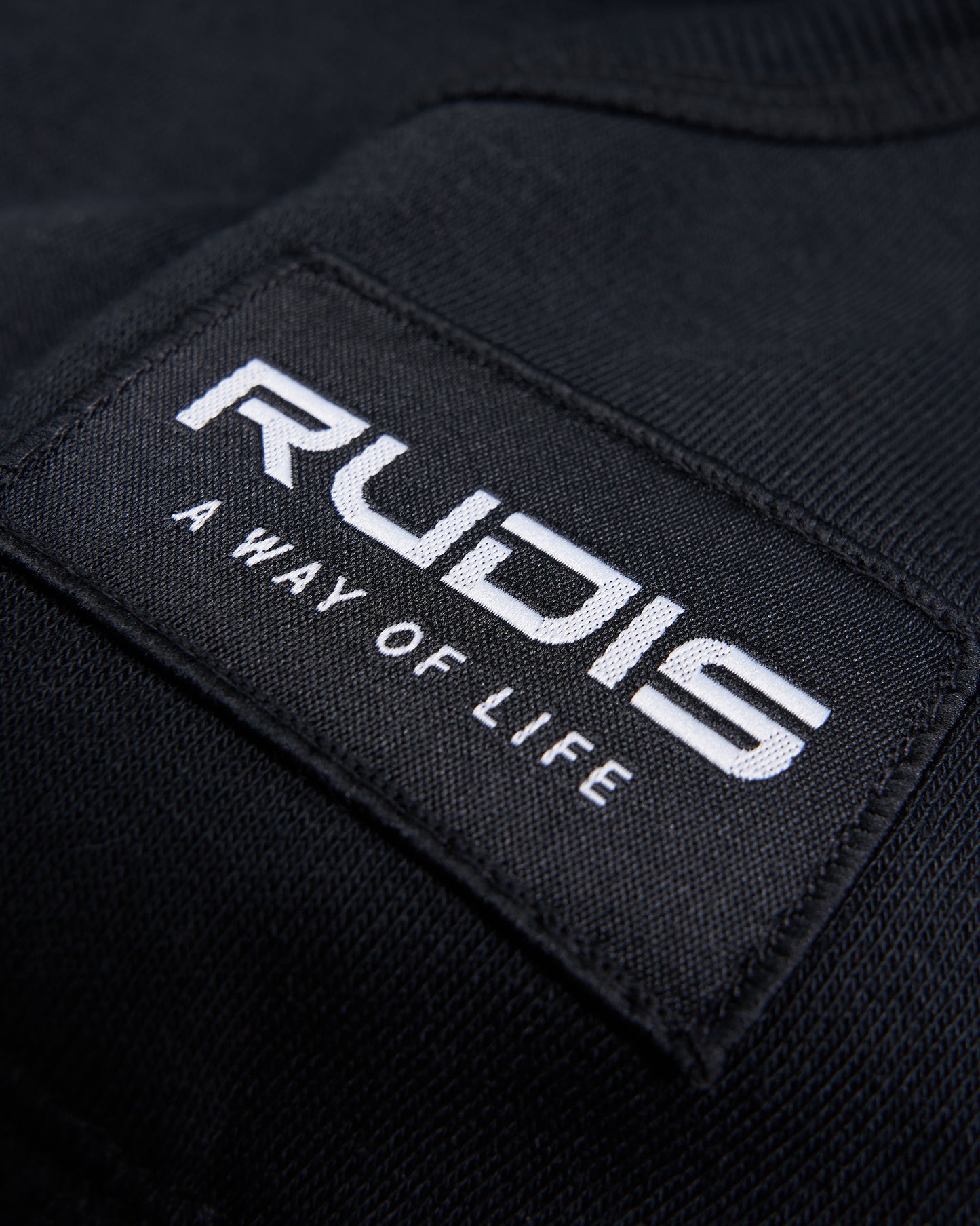 A close-up of a black fabric label featuring the brand name RUDIS and the tagline A WAY OF LIFE written in white