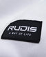 A close-up view of a black fabric label stitched onto a white garment featuring the text RUDIS and the slogan A WAY OF LIFE