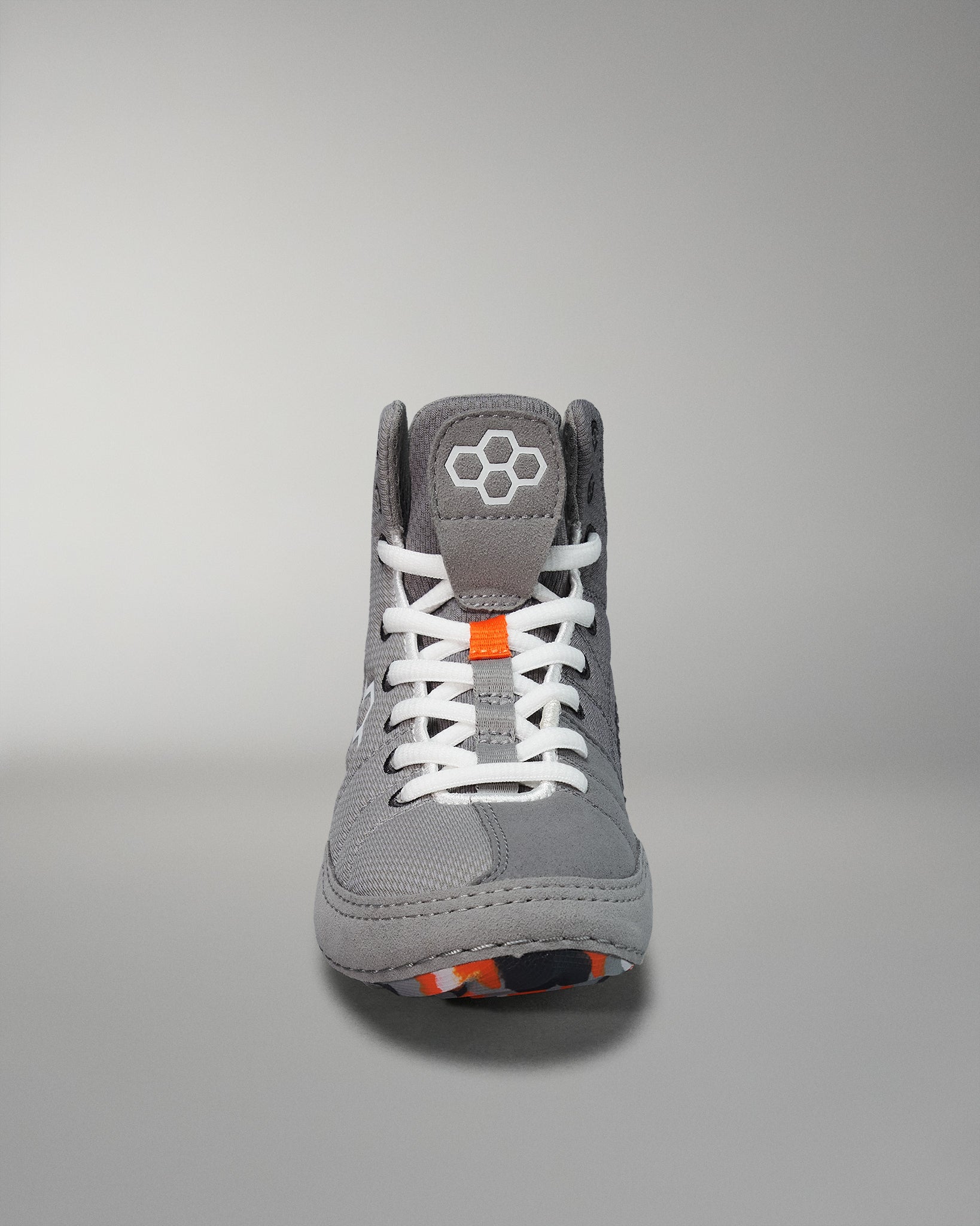 Front view of a gray athletic shoe showcases orange laces and a hexagonal logo, with a textured outsole emphasizing its active use design.