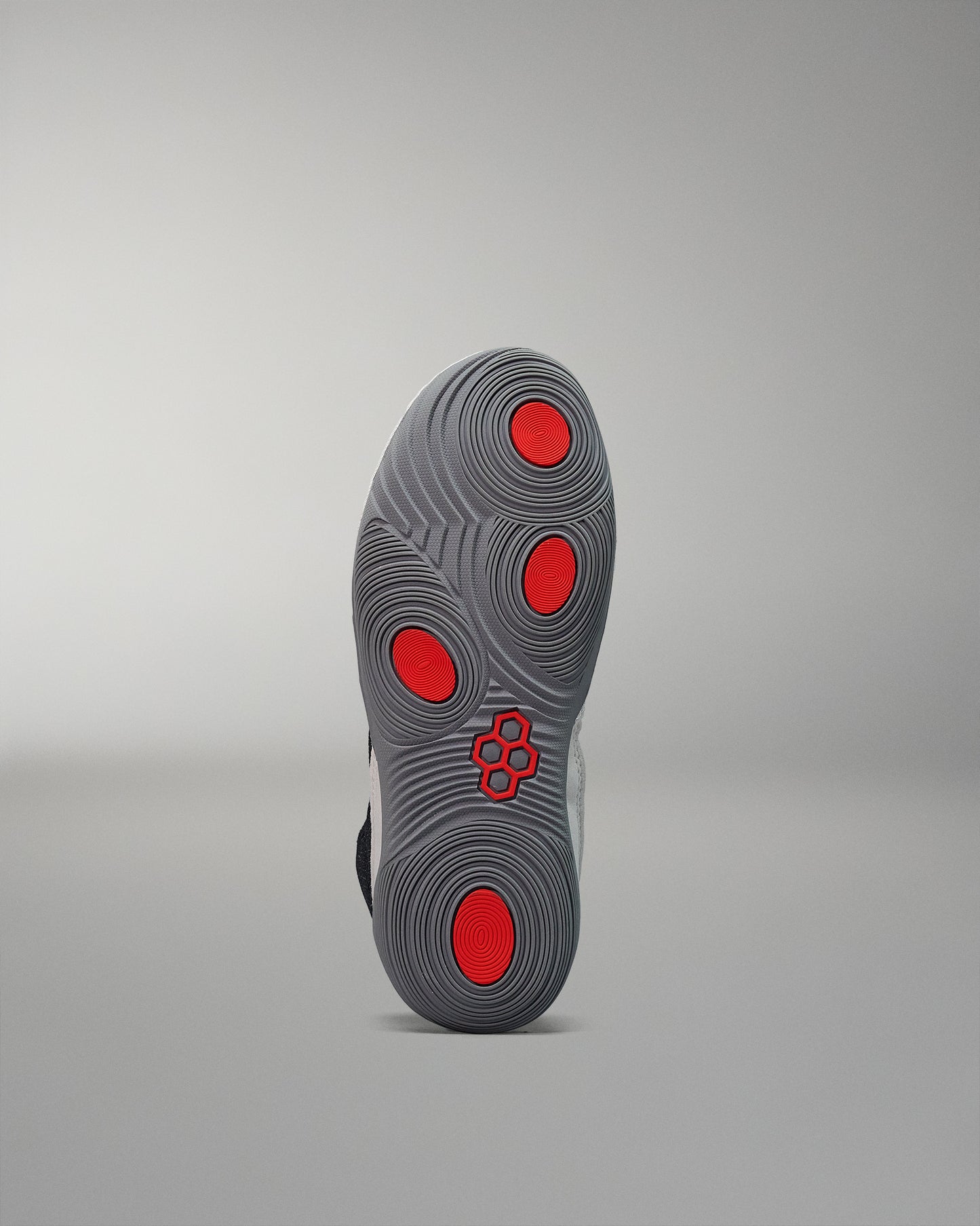 A shoe's sole displays intricate black and gray textures with red accents, designed for grip, set against a soft gray background.