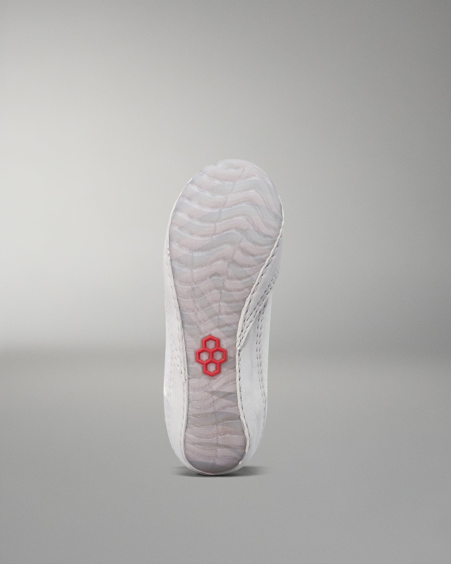 The underside of a shoe features a sleek white design with textured patterns for traction, complemented by a red hexagon logo against a soft gray background.