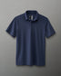 A navy blue polo shirt with a textured fabric, collared neckline, and an embossed logo on the shoulder against a neutral background.