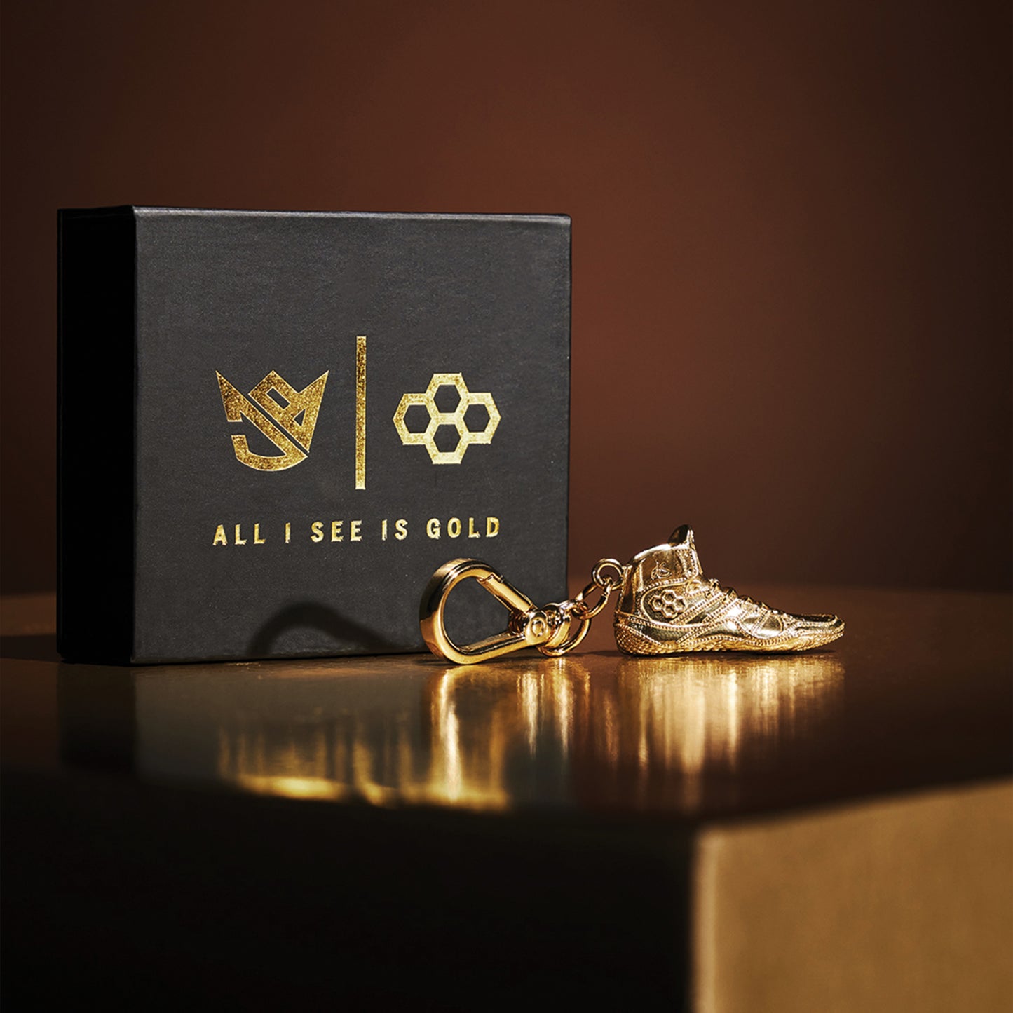 A golden sneaker keychain with intricate details accompanied by a stylish black box featuring a gold logo and the phrase ALL I SEE IS GOLD