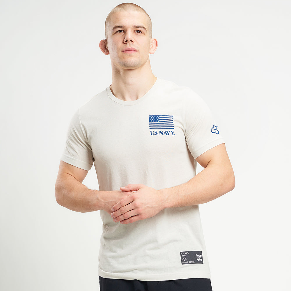 A model wearing a light-colored t-shirt featuring the US Navy logo and an American flag with a neutral background