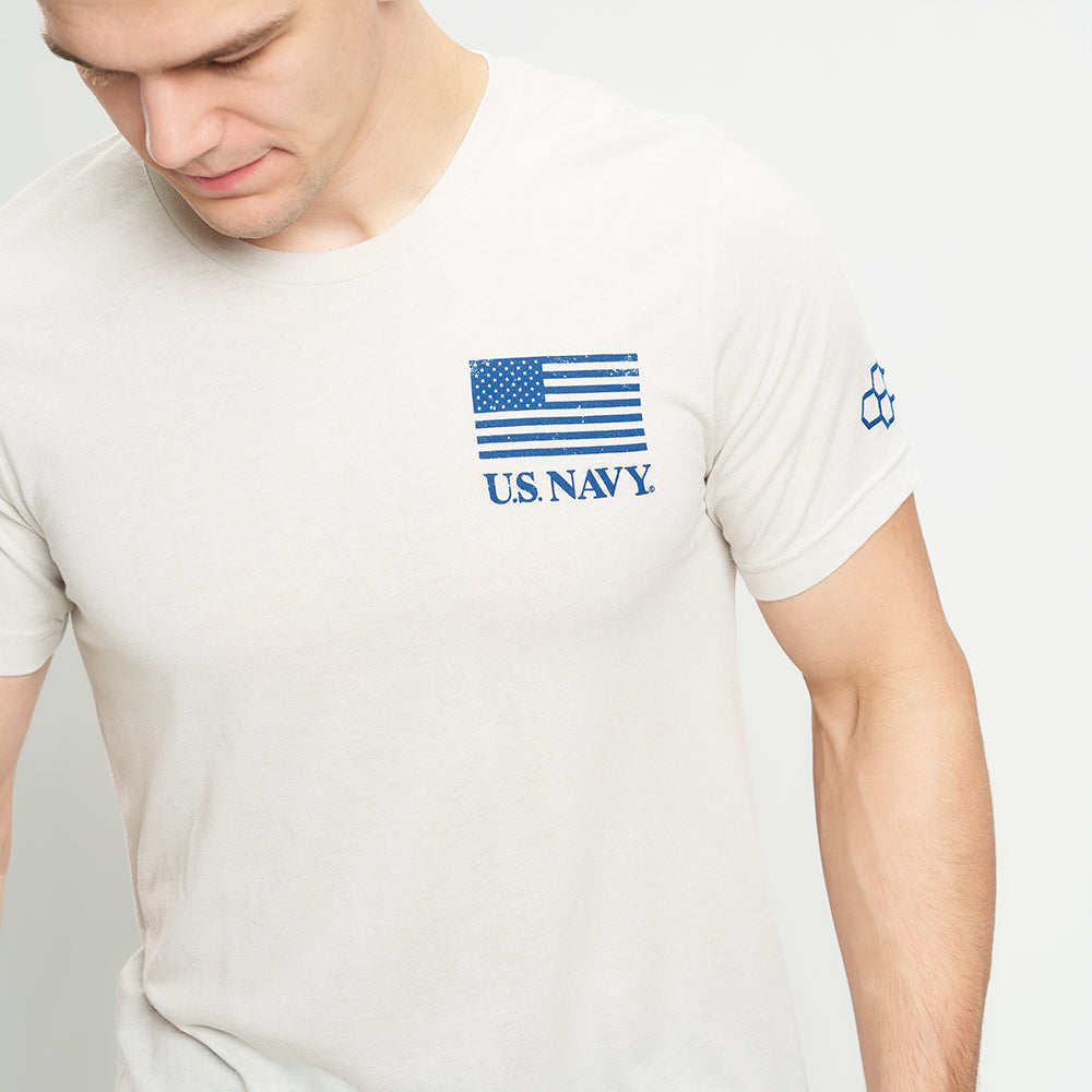 A close-up of a man wearing a light-colored t-shirt featuring a blue US Navy graphic with an American flag design on the front